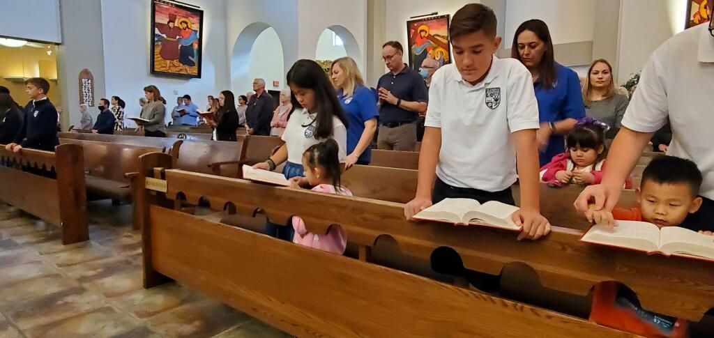 People seated in church pews during a service, with children and adults bowing their heads in prayer.