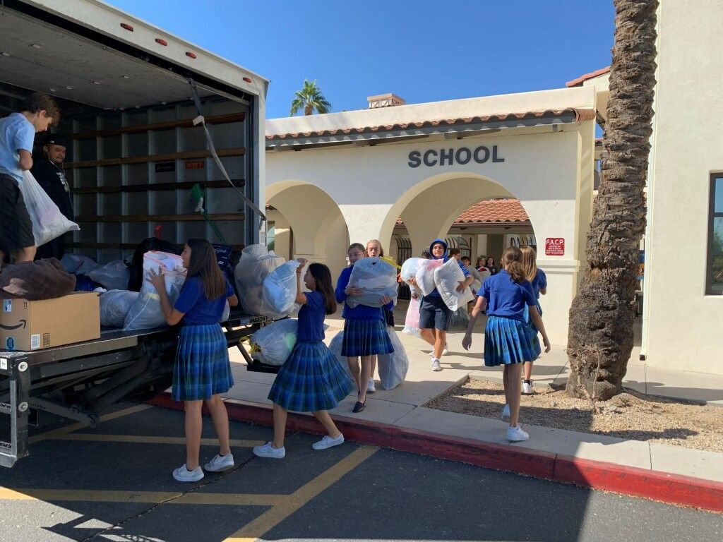 Students in blue uniforms gather outside a school entrance as boxes are unloaded from a truck.