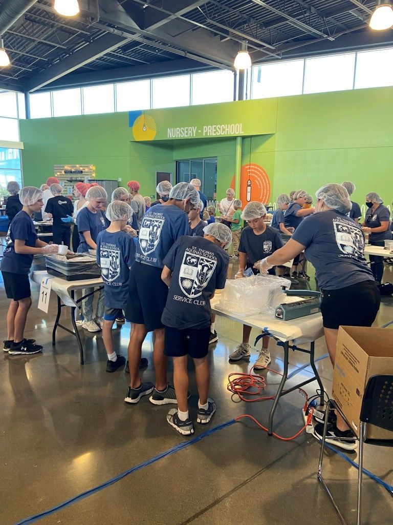 People gathered around tables at an indoor workshop with green walls and industrial ceiling lights.