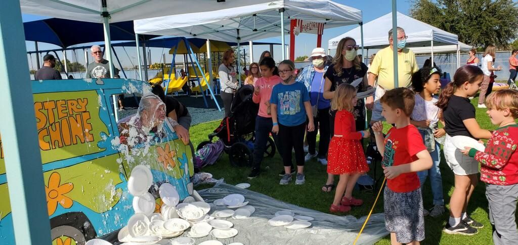 People gathered at an outdoor fair beside a colorful booth and display table on a sunny day