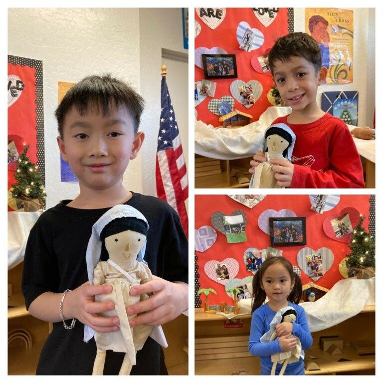 Three children at a holiday display, each holding a handmade doll craft.