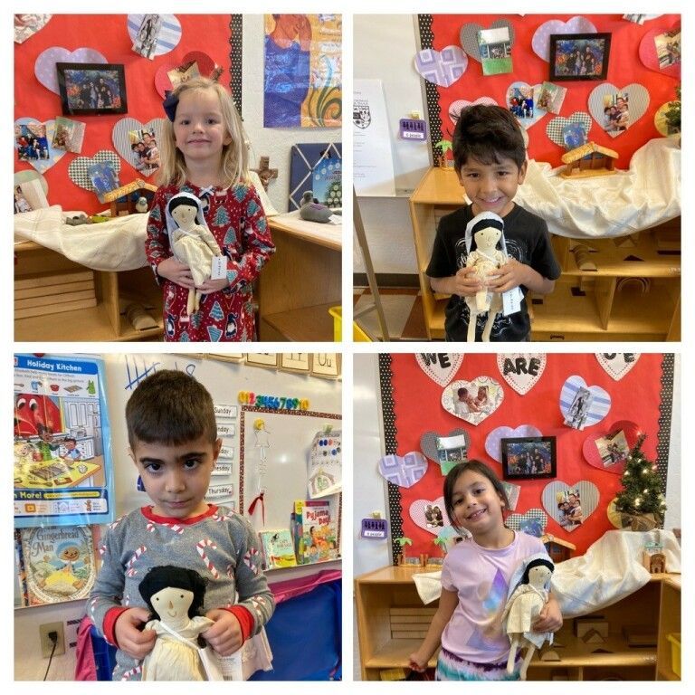 Four children holding dolls in a colorful classroom display, smiling and posing in front of red bulletin boards