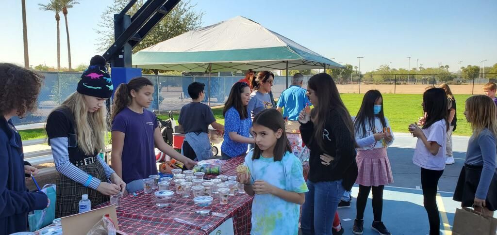 People gathered outdoors at a table with snacks and drinks under a sunny sky.