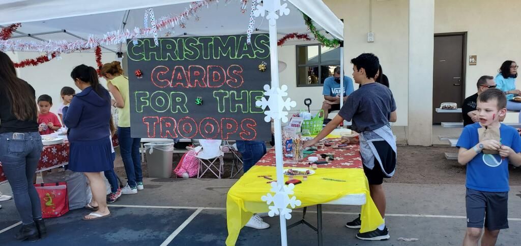 Outdoor Christmas craft booth with hanging tinsel, handmade signs, and people browsing tables