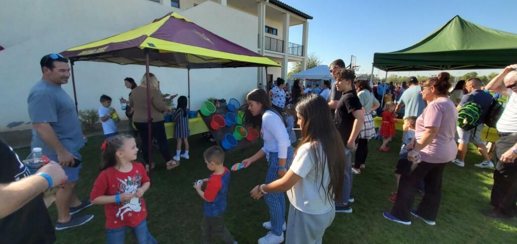 People gathered outdoors under green tents at a lively community event, with children playing on the grass.