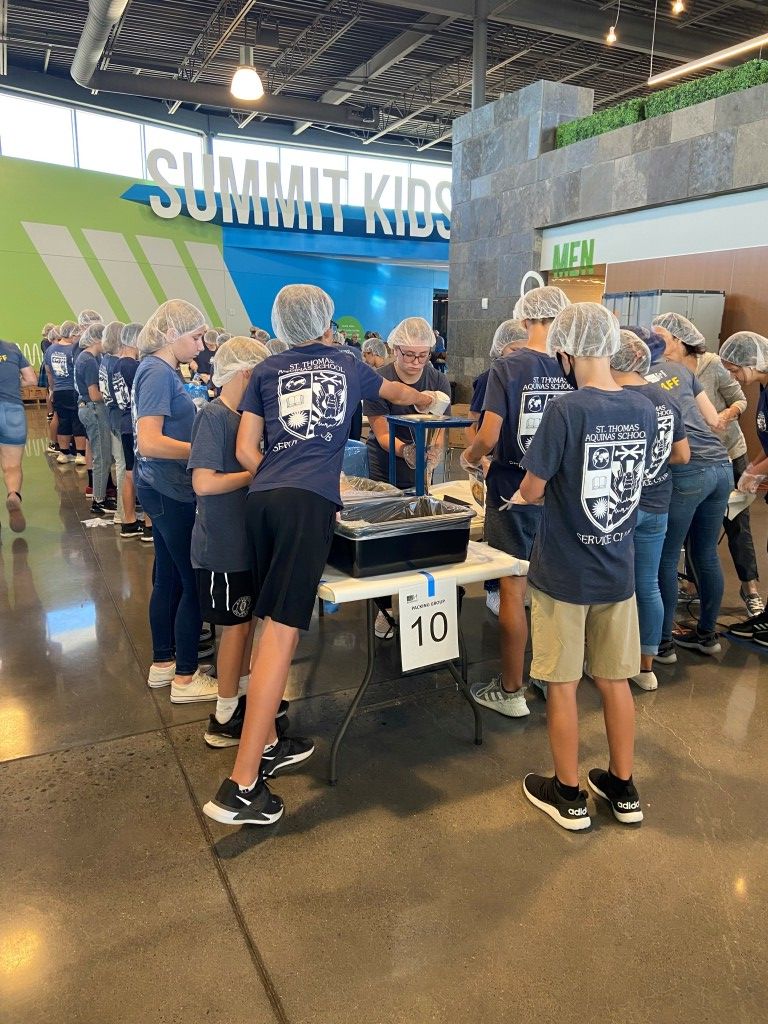 Group in navy shirts around a table at a busy indoor expo booth with a green sign overhead.