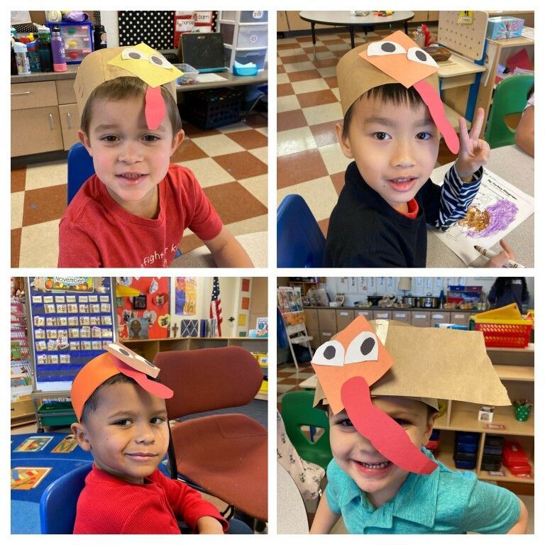 Four children in a classroom wearing handmade turkey hats and smiling at the camera.