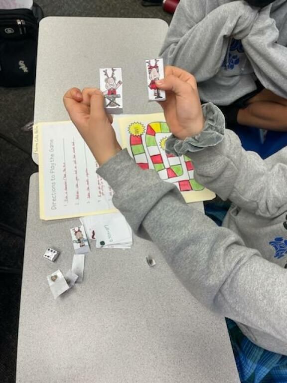 Hands working on a classroom tabletop game with colorful cards and a worksheet.