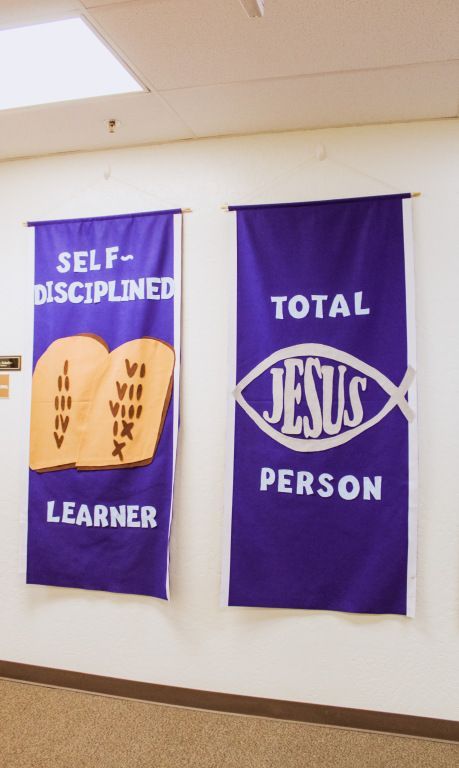 Purple wall banners reading “Self-Disciplined Learner” and “Total Jesus Person” hanging indoors.