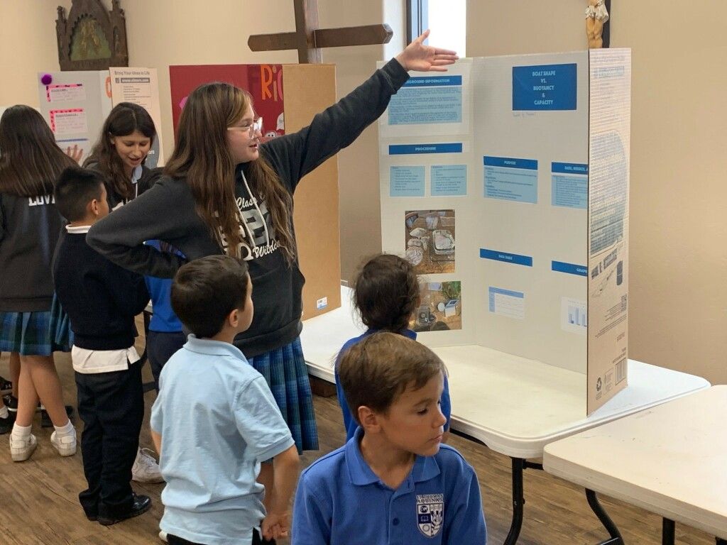 Children gathered around a classroom poster, one pointing to display panels during a group activity.