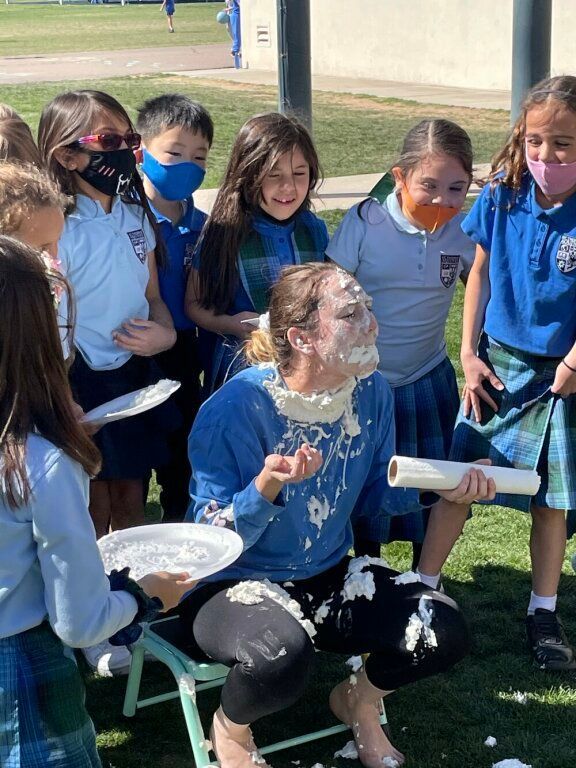 Students at school dumping white foam over a seated person outdoors.