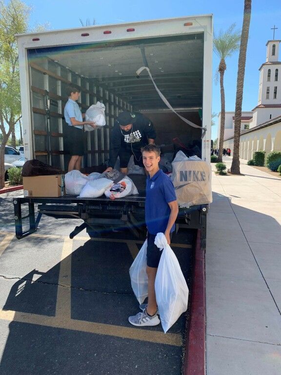Person unloading bags from a truck at a church entrance, with another person inside the truck and a bell tower nearby