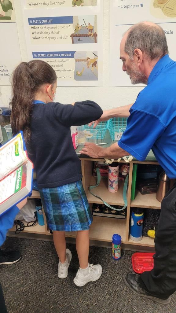 Teacher and child examining a colorful classroom display near shelves and posters