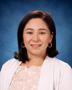 Portrait of a smiling person in a white cardigan against a blue studio background