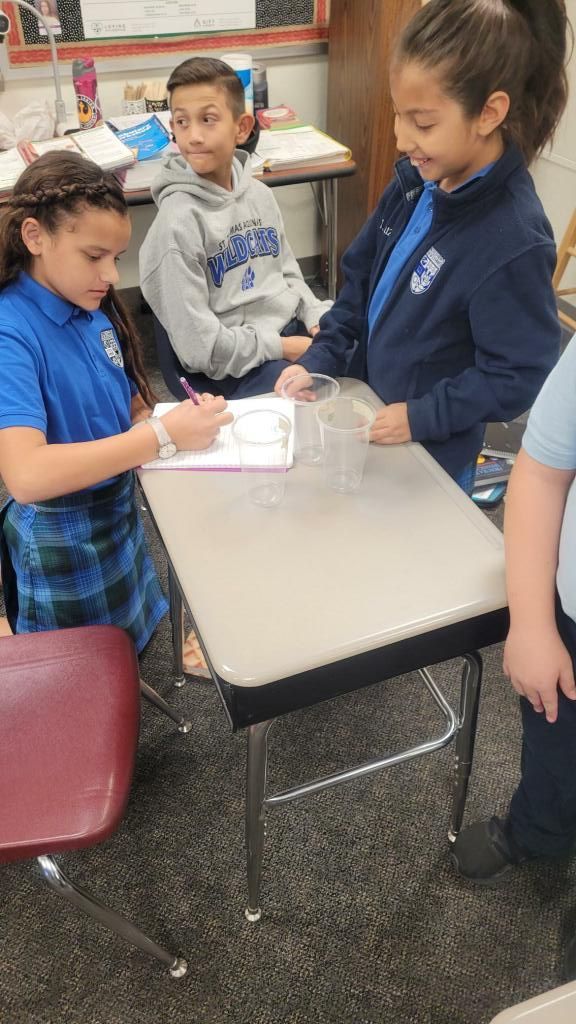 Students gather around a classroom table, working together on a hands-on activity.