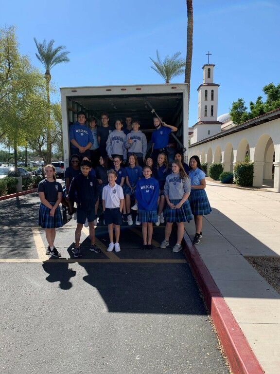 Group of students in blue uniforms posing outside a truck, with a church tower in the background