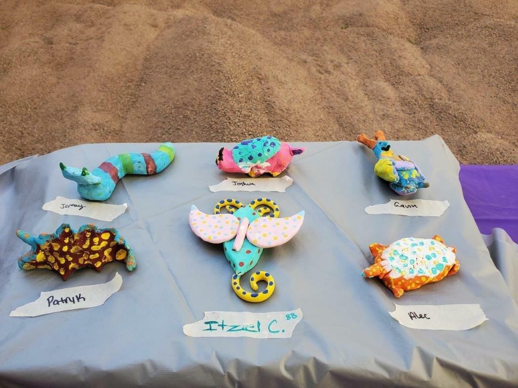 Colorful handmade craft pieces displayed on a gray tablecloth at an outdoor market.