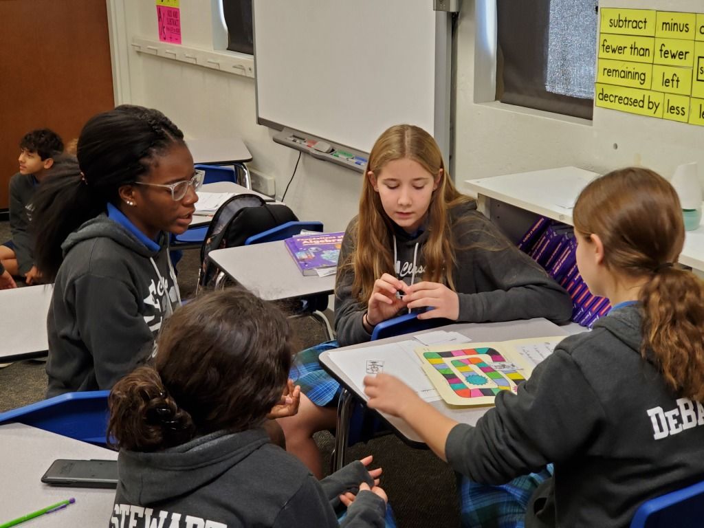 Students gather around a classroom table, working together on a colorful activity sheet.