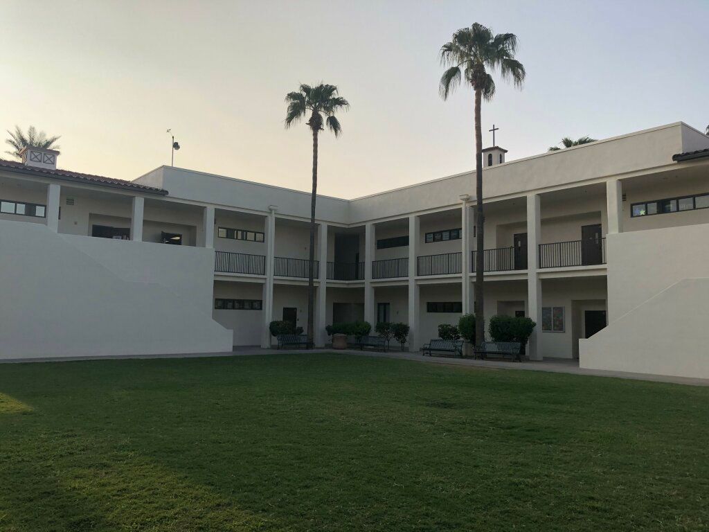 Modern white courtyard building with a green lawn and tall palm trees at sunset