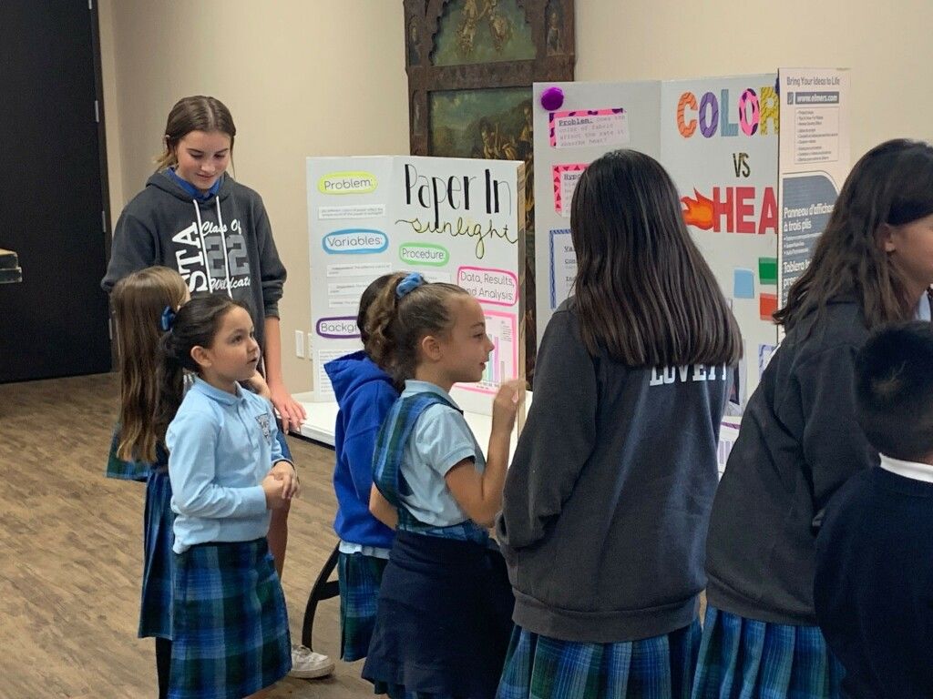 Children and a teacher gather in a classroom around colorful posters on the wall.