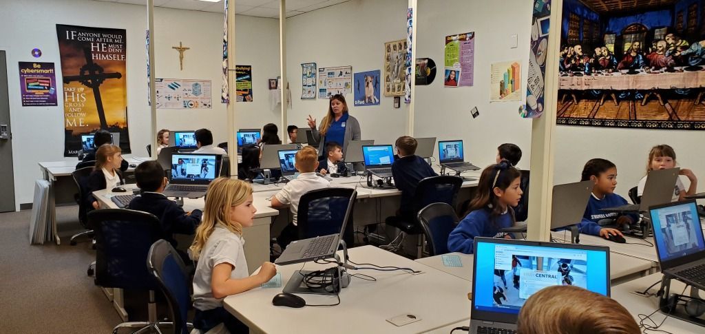 Classroom with students working at desks on laptops and papers during a lesson