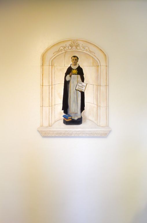 Painted saint statue in a wall niche with an arched frame on a pale wall