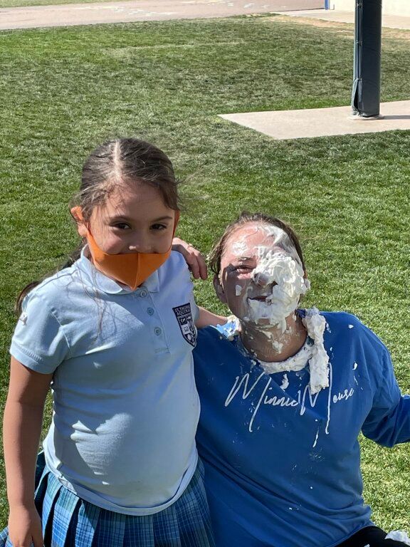 Two people outdoors with pie on their faces and shirts, standing on grass near a walkway.