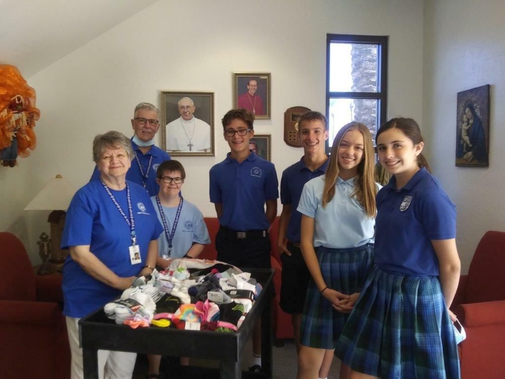 Group of people in blue shirts standing indoors around a table with colorful items
