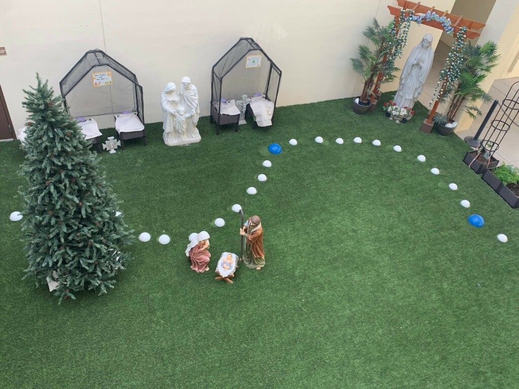 Miniature holiday village with small houses, evergreen trees, and tiny figurines on green artificial grass.
