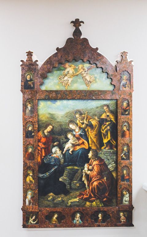 Ornate framed religious painting with figures gathered around a central scene in rich colors.