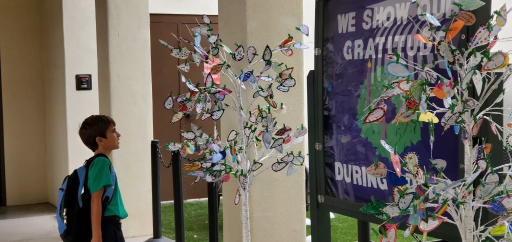 Child with backpack looking at colorful paper butterflies on a wall display in a school hallway