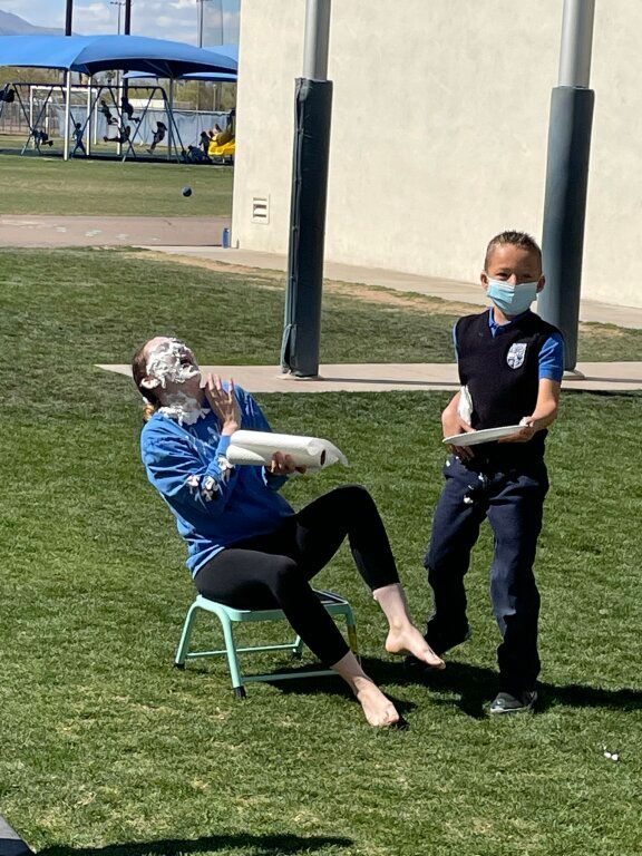Woman seated on a small chair and boy standing beside her outdoors on grass, both wearing masks