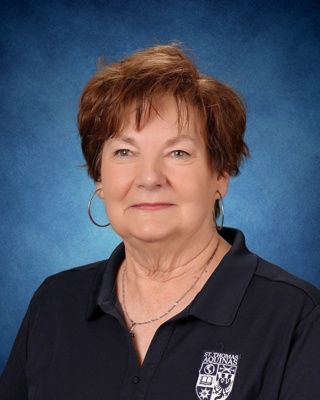 Head-and-shoulders portrait of a smiling person in a navy blouse on a blue studio background