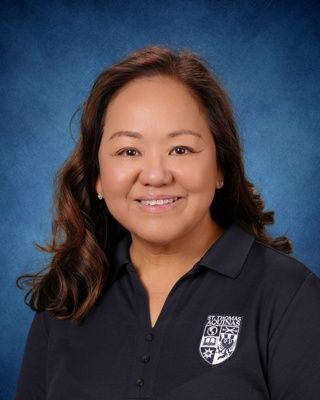 Smiling woman in a beige blouse and beaded necklace against a blue studio backdrop