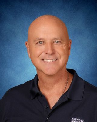 Head-and-shoulders portrait of a smiling person in a navy blouse on a blue studio background