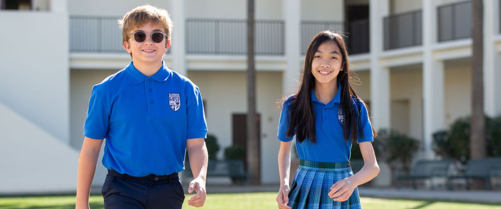 Two children in blue school uniforms walking outside a school building