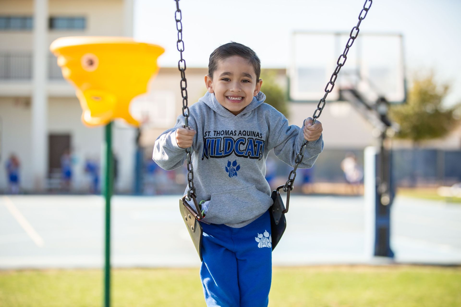 Child smiling on a swing at a playground, with a yellow slide in the background.