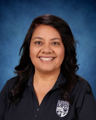 Smiling woman with curly brown hair in a black floral top against a blue studio backdrop