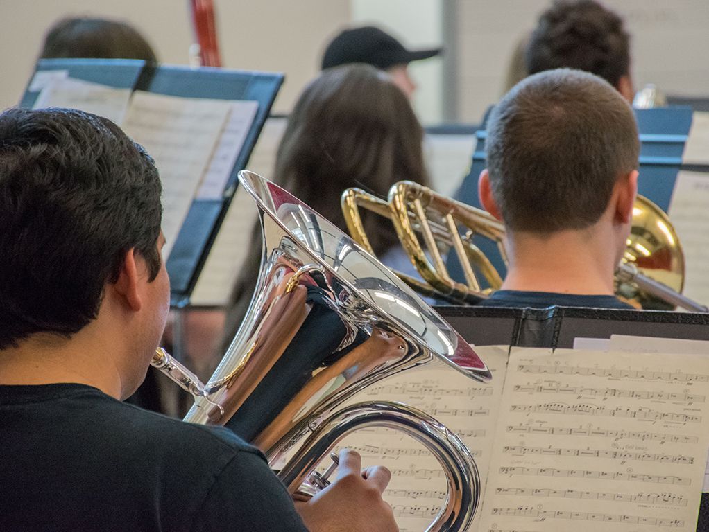 Musicians seated in an orchestra rehearsal, holding brass instruments and reading sheet music