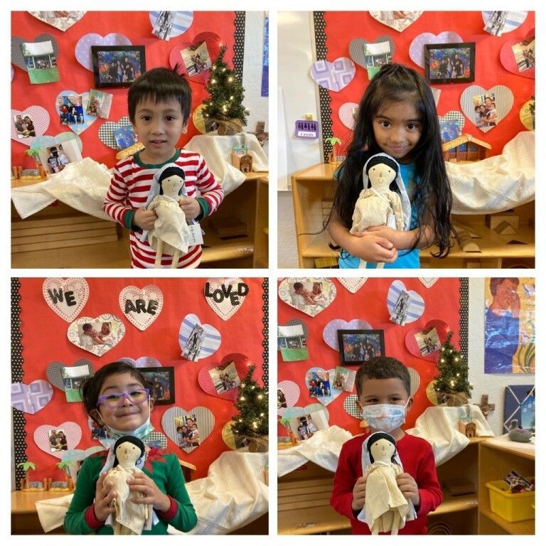 Four children hold dolls in a classroom Valentine display with red hearts and decorations.