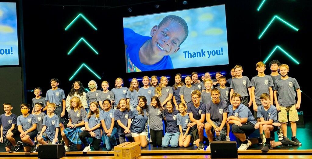 Large group of people posing on stage in matching shirts, with a screen reading “Thank you!” in the background