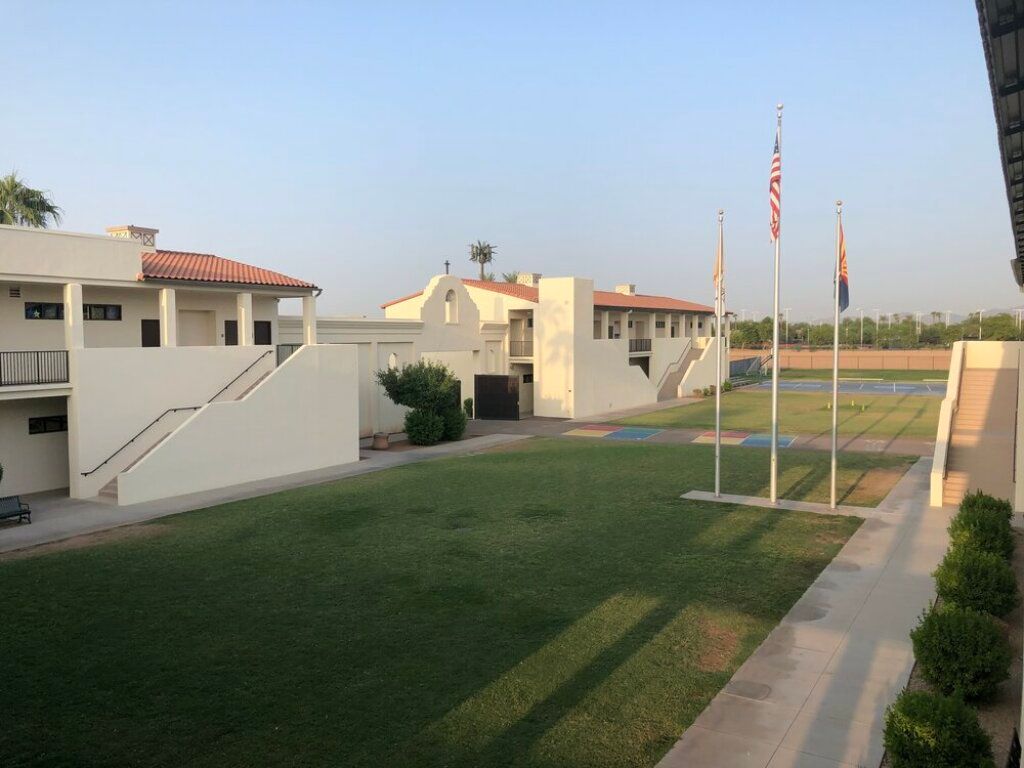 Courtyard of white buildings with green lawn and flagpoles at a small campus or hotel