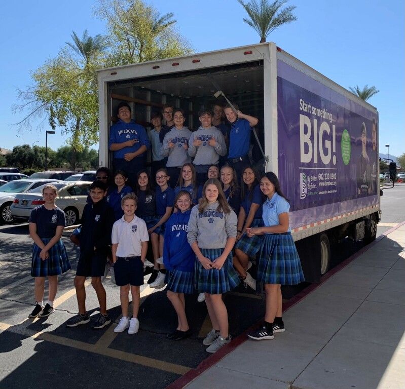 Group posing beside a purple BIG1 truck, with students in blue and plaid uniforms outdoors on a sunny day.