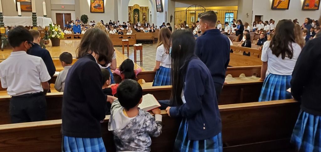 People standing in a church pew during a service, facing the altar.