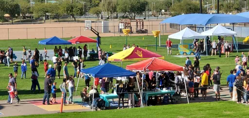 Crowd at a park event with colorful tents and tables on a grassy field