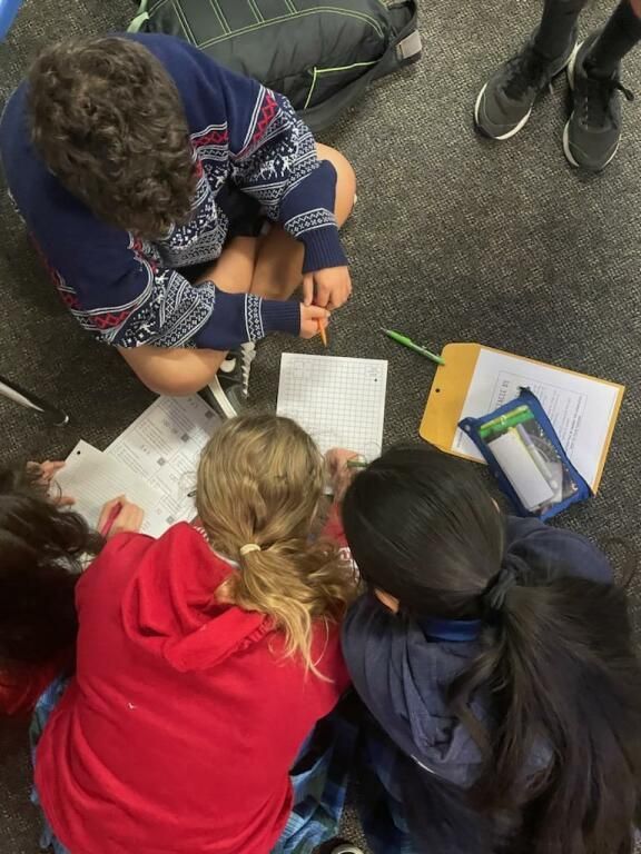 Three people sit on the floor collaborating over papers and a yellow folder in a classroom.