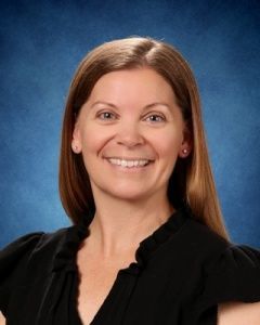 Smiling woman in a black blouse against a blue studio backdrop.