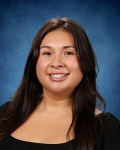 Smiling person with long dark hair against a blue studio backdrop, wearing a black top.