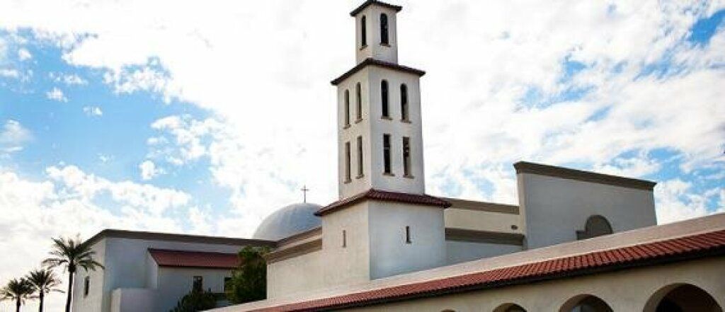White church with a tall bell tower and dome under a partly cloudy blue sky