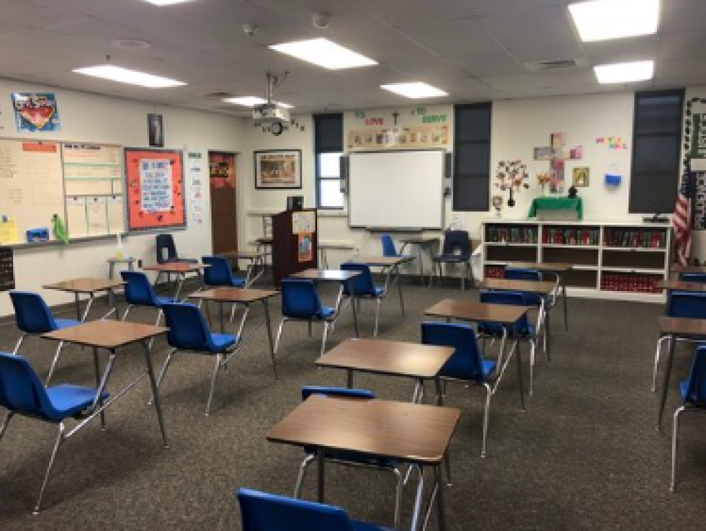 Empty classroom with blue chairs and desks arranged in rows, projector screen at the front.